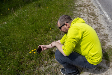 A man in a vibrant yellow shirt and cap is crouched down in a field of green grass and yellow...