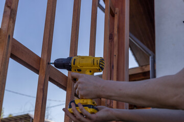 A person is using a drill to attach a wooden fence in a backyard setting. The drill bit is visible...