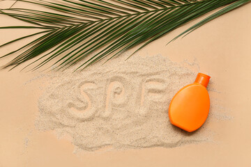 Bottle of sunscreen cream and word SPF made of sand on brown background