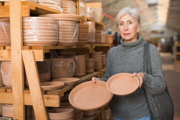 Portrait of modern aged woman choosing pots for house plants in gardening market..
