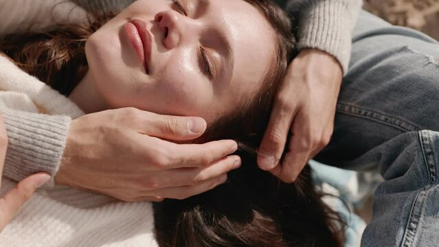 A moment of trust and affection as a young woman lies with closed eyes on the knees of her partner, feeling the warmth of love and care outdoors.