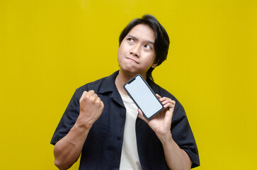 mock up young Asian man showing and pointing at blank screen smartphone. asian man in beige tshirt...