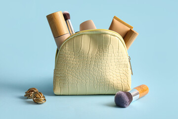 Yellow cosmetic bag with makeup products, earrings and brushes on blue background