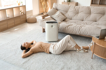 Young woman lying on floor near humidifier in beautiful living room