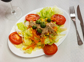 Plate is beautifully stacked with large pieces of fresh vegetables, cabbage, carrots and tuna fillets. Salad is decorated with green olives and complemented with saucer with fresh baguette