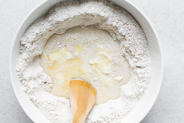 Overhead view of hot cross bun dough being mixed in a white mixing bowl, process of making hot cross buns