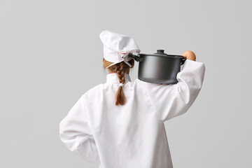 Teenage chef with cooking pot on grey background, back view