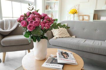 Vase with pink roses and magazines on table in living room, closeup