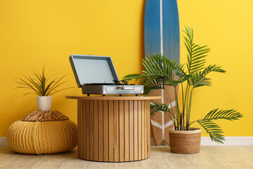 Coffee table, record player, houseplants and surf board near yellow wall in room