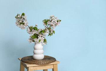 Vase with blossoming branches on coffee table near blue wall in room