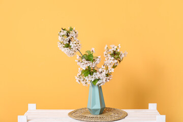 Vase with blossoming branches on shelf near orange wall in room