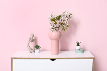 Vase with blossoming branches on table near pink wall in room