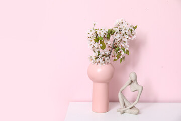 Vase with blossoming branches on table near pink wall in room