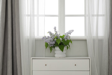 White vase with beautiful bouquet of flowers on chest of drawers near window