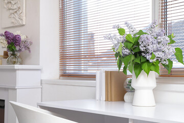 Vase with flowers and books on table near window in living room