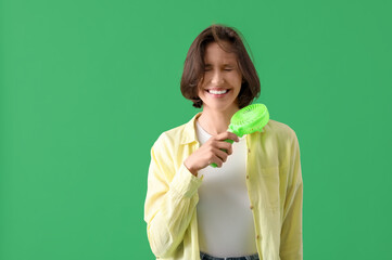Young woman with portable electric fan on green background