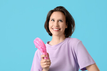 Young woman with pink portable electric fan on blue background