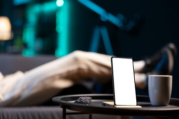 Focus on mockup device with man sleeping on couch in blurry background in neon lit apartment. Close...