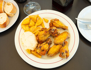 Close-up of snack dish. There is plate with fried chicken wings and portion of French fries and...