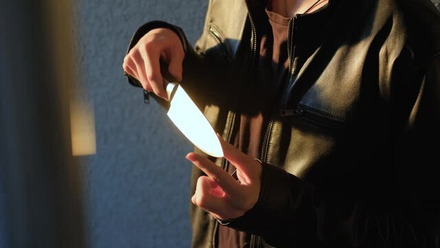An unrecognizable criminal takes out a knife from under his clothes, close-up