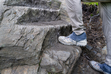 Man's hiking boots with gaiters and pants climbing steps cut in rock along the Alum Cave Trail,...