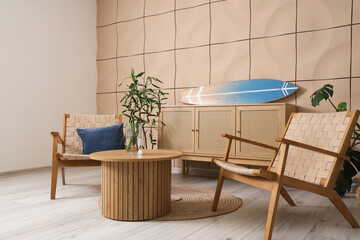 Interior of living room with surfboard on commode, table and armchairs