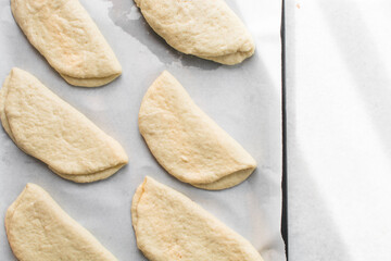 Coco bread dough rising on a parchment lined baking tray, shaped coco bread about to be baked, process of making jamaican coco bread