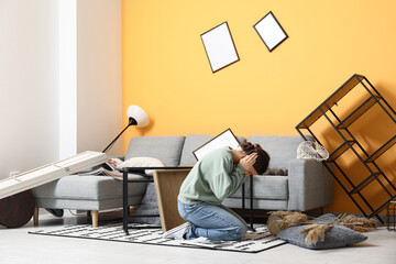 Young woman sitting on floor in living room with messed furniture after earthquake
