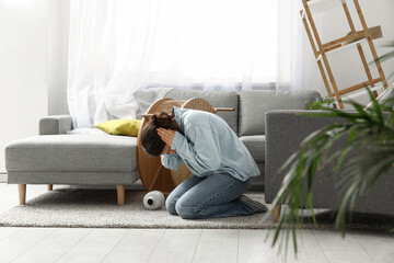 Young woman sitting on floor in living room with messed furniture after strong earthquake