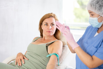 Portrait of Asian-looking doctor giving injection in arm to patient lying on couch