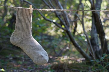 Lone knitted sock dries on a clothesline amidst a natural green background