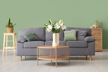 Interior of stylish living room with bouquet of lily flowers on coffee table, pillows and cozy sofa