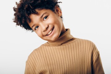 joyful african american boy in brown turtleneck sweater beaming with a bright smile against a white...