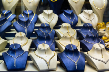 Assortment of jewelry is presented in brightly lit shop window. There are necklaces, sets of...