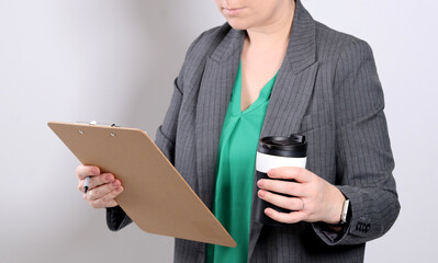 Close up of a business woman holding a clipboard and a cup of coffee, grey empty studio background