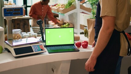 Shop owner works with greenscreen on laptop, sitting at register counter and waiting to serve...