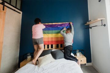 lgbt lesbian latin couple on bed at home in Mexico, Hispanic homosexual people from lgbtq community with rainbow flag in Latin America	