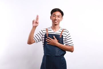Asian young man wearing apron over white background smiling swearing with hand on chest and fingers...