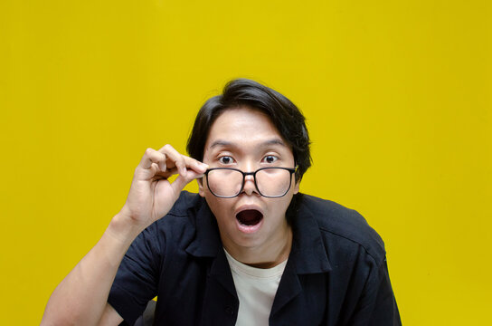 funny expression young asian man shocked happily opening mouth and lowering glasses. asian man with glasses feels shock with wow surprised expression.