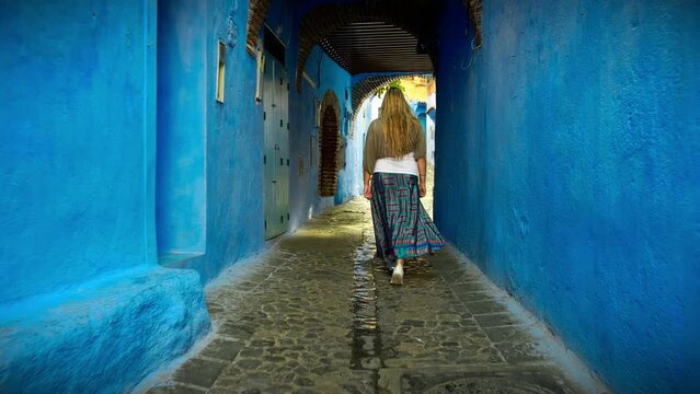 European blonde girl walking in Medina alleys and stairs of Chefchaouen, the famous Blue Pearl of Morocco or Blue City. Chaouen is noted for its buildings in shades of blue, UNESCO heritage.