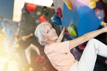 Confident mature woman scaling artificial climbing wall in climbing gym