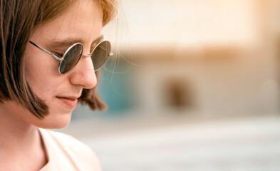 A stylish young girl in black sunglasses walks in a city, portrait closeup.