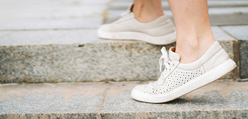 A girl walks up the stairs in the city outdoors, legs in the sneakers closeup.