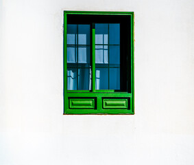 A white rural house with a green wooden window frame in a daylight.