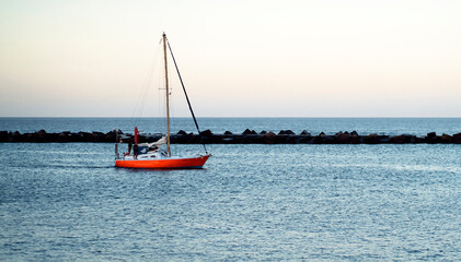 A red yacht sails across the Atlantic Ocean at sunset.