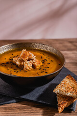 bowl of golden pumpkin soup with croutons and sesame seeds on top over slate boards and wooden rustic table 