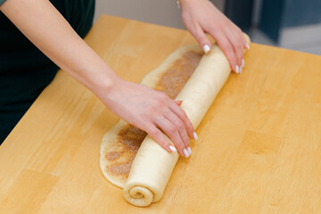 One Caucasian young girl rolls cinnamon dough into a roll on the table.