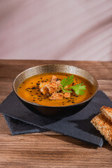 bowl of golden pumpkin soup with croutons and sesame seeds on top over slate boards and wooden rustic table 