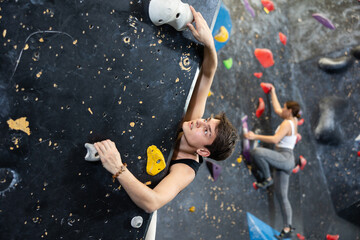 Sporty young guy doing a difficult wall climb in climbing gym