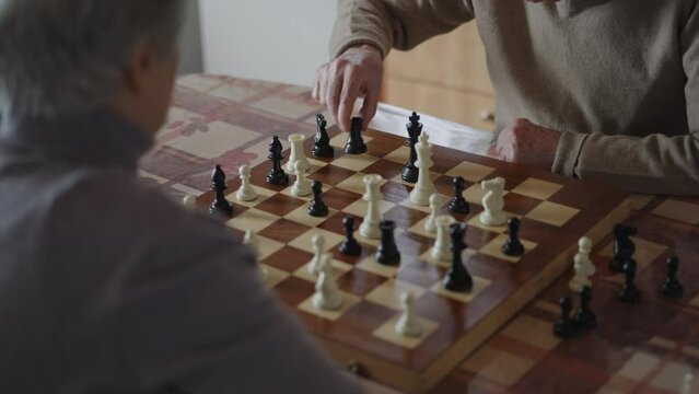 An elderly couple intensely focusing on a chess game at a table in their village home, with a warm fireplace in the background.